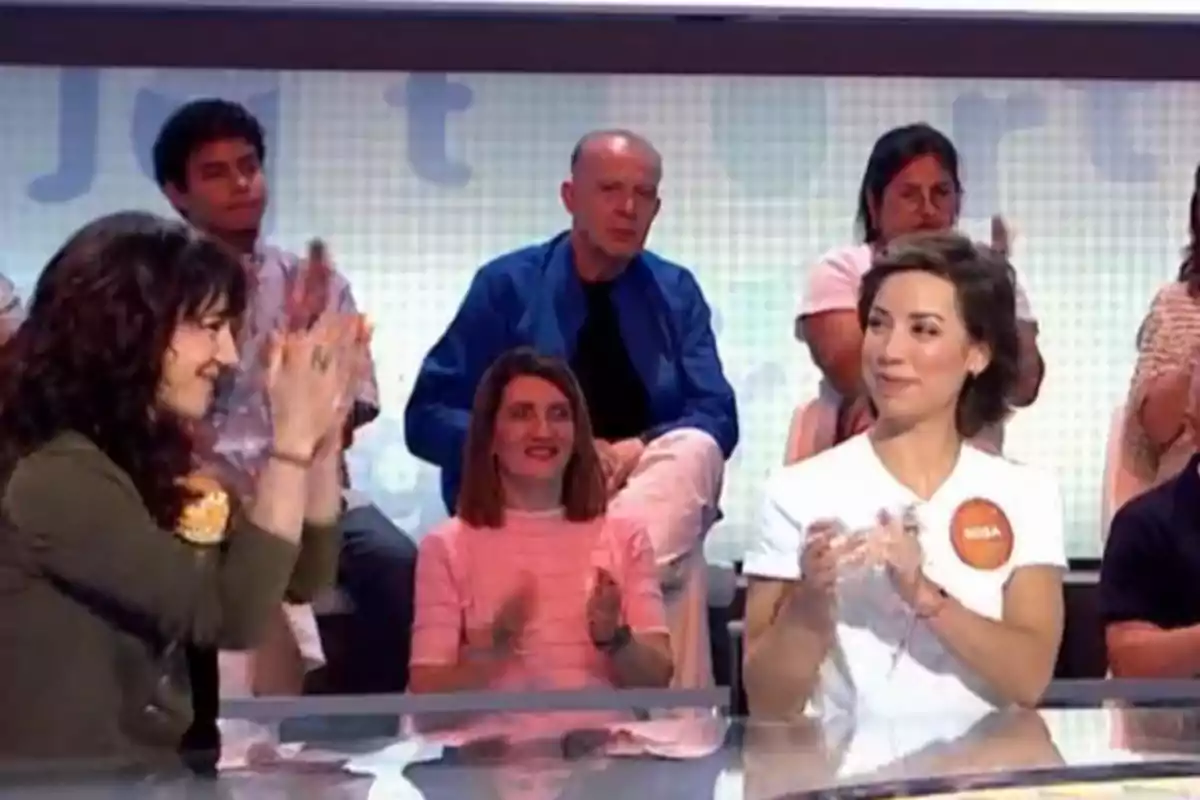Two women sitting on a television set applaud while the audience watches them. Two women sitting on a television set applaud while the audience watches them.