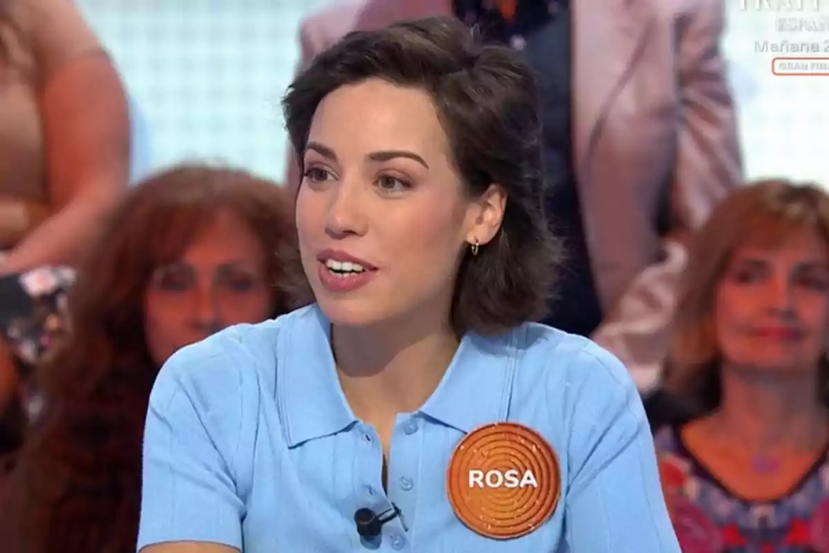 Dona de cabell curt i fosc amb una camisa blau clar i una acreditació que diu Rosa participant en un programa de televisió amb públic al fons Dona de cabell curt i fosc amb una camisa blau clar i una acreditació que diu Rosa participant en un programa de televisió amb públic al fons