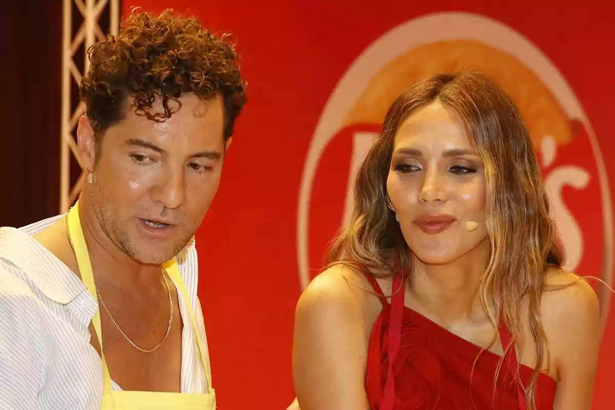 David Bisbal y Rosanna Zanetti participando en un evento culinario con fondo rojo y logotipo detrás David Bisbal y Rosanna Zanetti participando en un evento culinario con fondo rojo y logotipo detrás