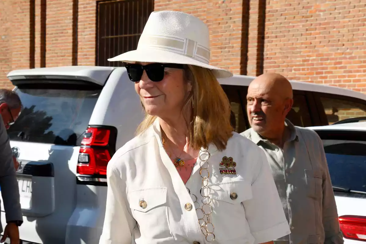 La Infanta Elena, en una imatge d'arxiu, amb barret blanc i ulleres de sol, somriu a l'aire lliure al costat d'un home, tots dos davant d'un cotxe blanc i una paret de maó. La Infanta Elena, en una imatge d'arxiu, amb barret blanc i ulleres de sol, somriu a l'aire lliure al costat d'un home, tots dos davant d'un cotxe blanc i una paret de maó.