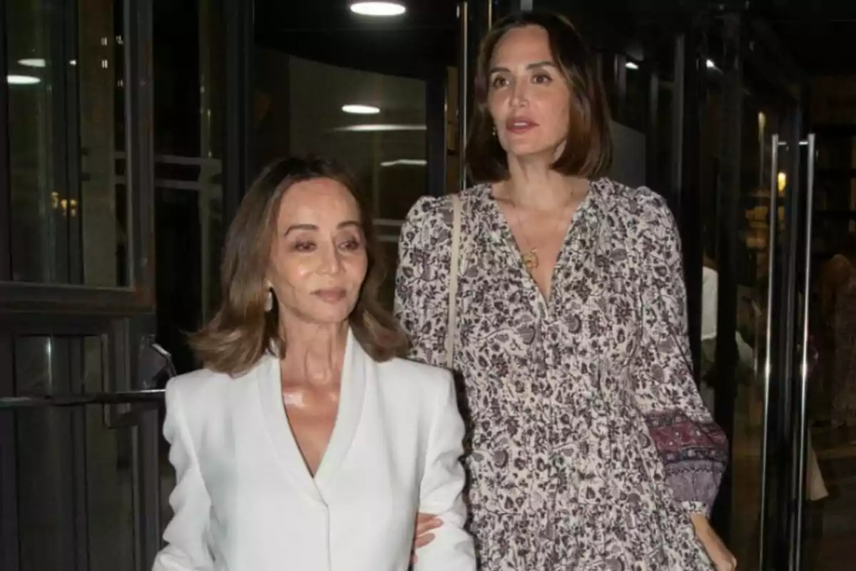 Isabel Preysler i Tamara Falcó, elegantment vestides, surten d’un edifici per una porta de vidre; una porta un conjunt blanc i l’altra un vestit estampat.