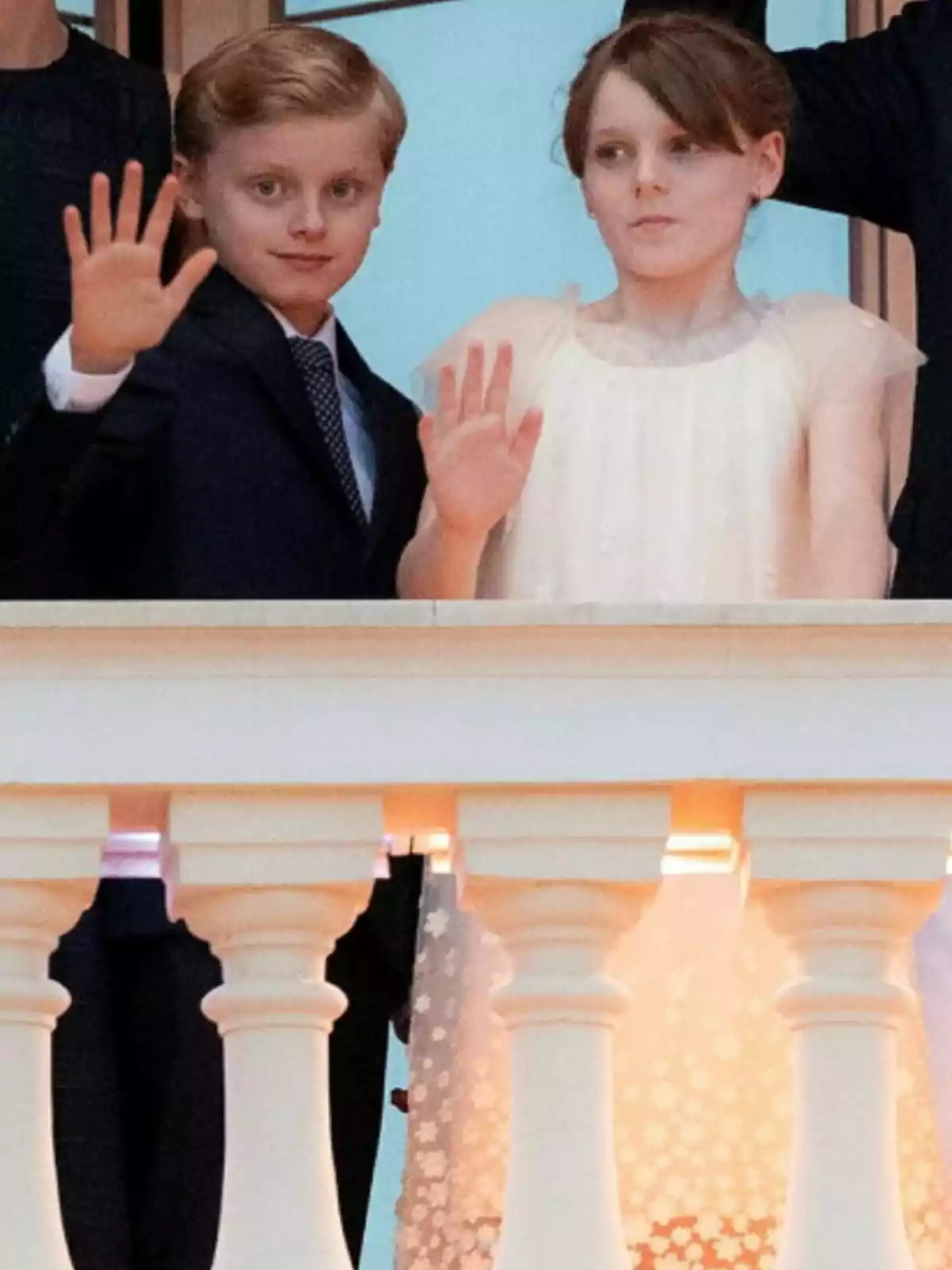 Dos nens elegantment vestits saluden des d’un balcó Dos nens elegantment vestits saluden des d’un balcó