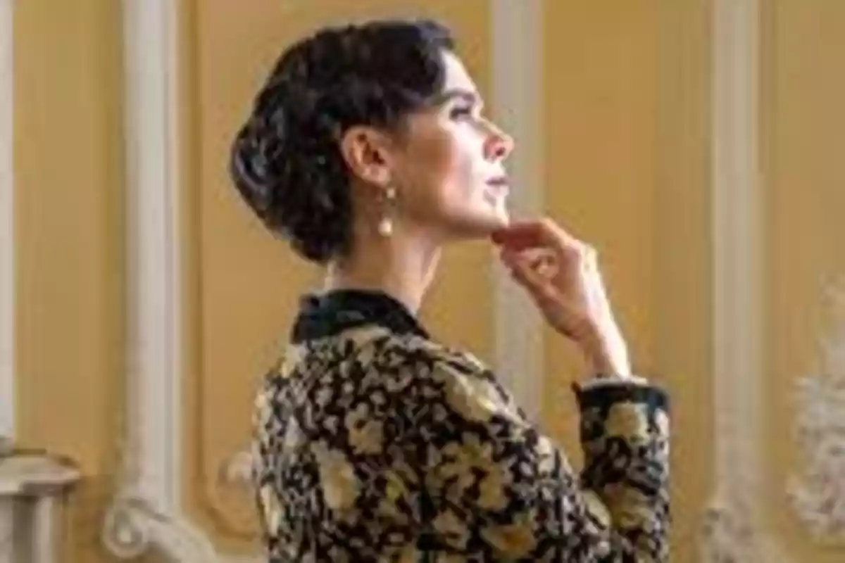 Esmeralda elegant de perfil amb els cabells recollits i un abric de flors daurades en un ambient clàssic. Captura de 'La Promesa' Esmeralda elegant de perfil amb els cabells recollits i un abric de flors daurades en un ambient clàssic. Captura de 'La Promesa'