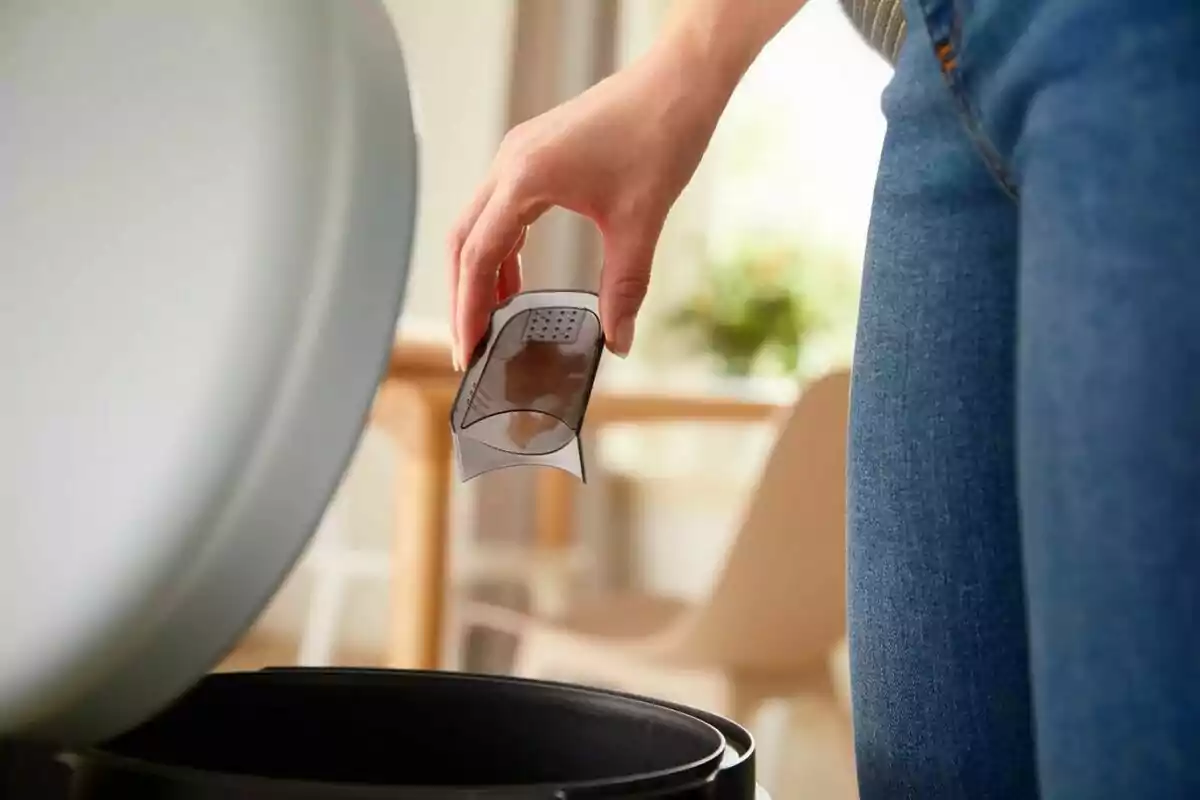 Persona llençant un filtre de cafè usat a una paperera a una cuina. Persona llençant un filtre de cafè usat a una paperera a una cuina.
