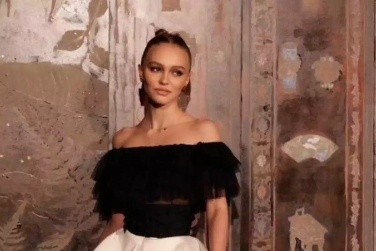 Lily-Rose Melody Depp dressed in an elegant off-the-shoulder black and white dress posing in front of a decorated wall. Lily-Rose Melody Depp dressed in an elegant off-the-shoulder black and white dress posing in front of a decorated wall.