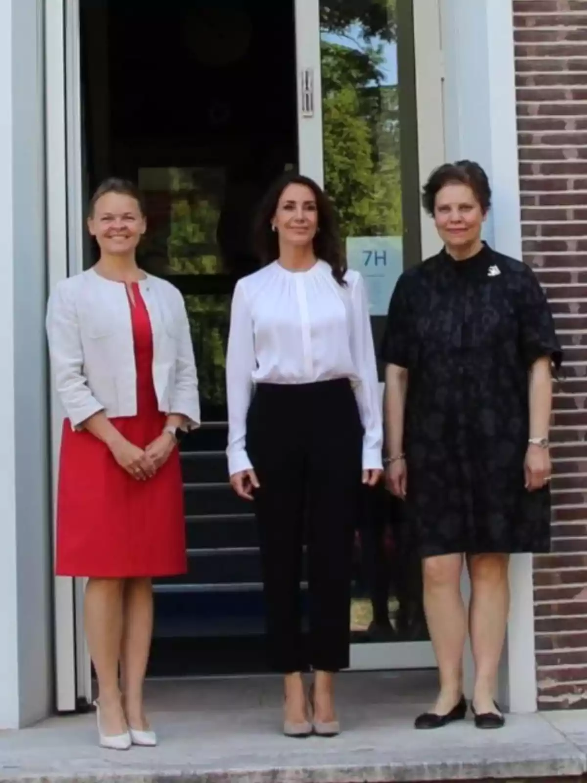 Tres dones posen dretes davant d’una porta d’entrada, totes vestides de manera formal i somrient a la càmera. Tres dones posen dretes davant d’una porta d’entrada, totes vestides de manera formal i somrient a la càmera.