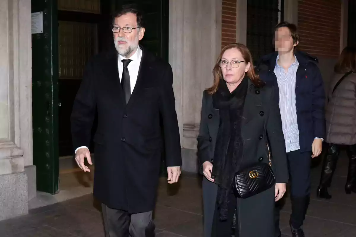 Maríano Rajoy i Elvira Fernández vestits de negre caminen junts pel carrer, acompanyats per una altra persona més al fons. Maríano Rajoy i Elvira Fernández vestits de negre caminen junts pel carrer, acompanyats per una altra persona més al fons.