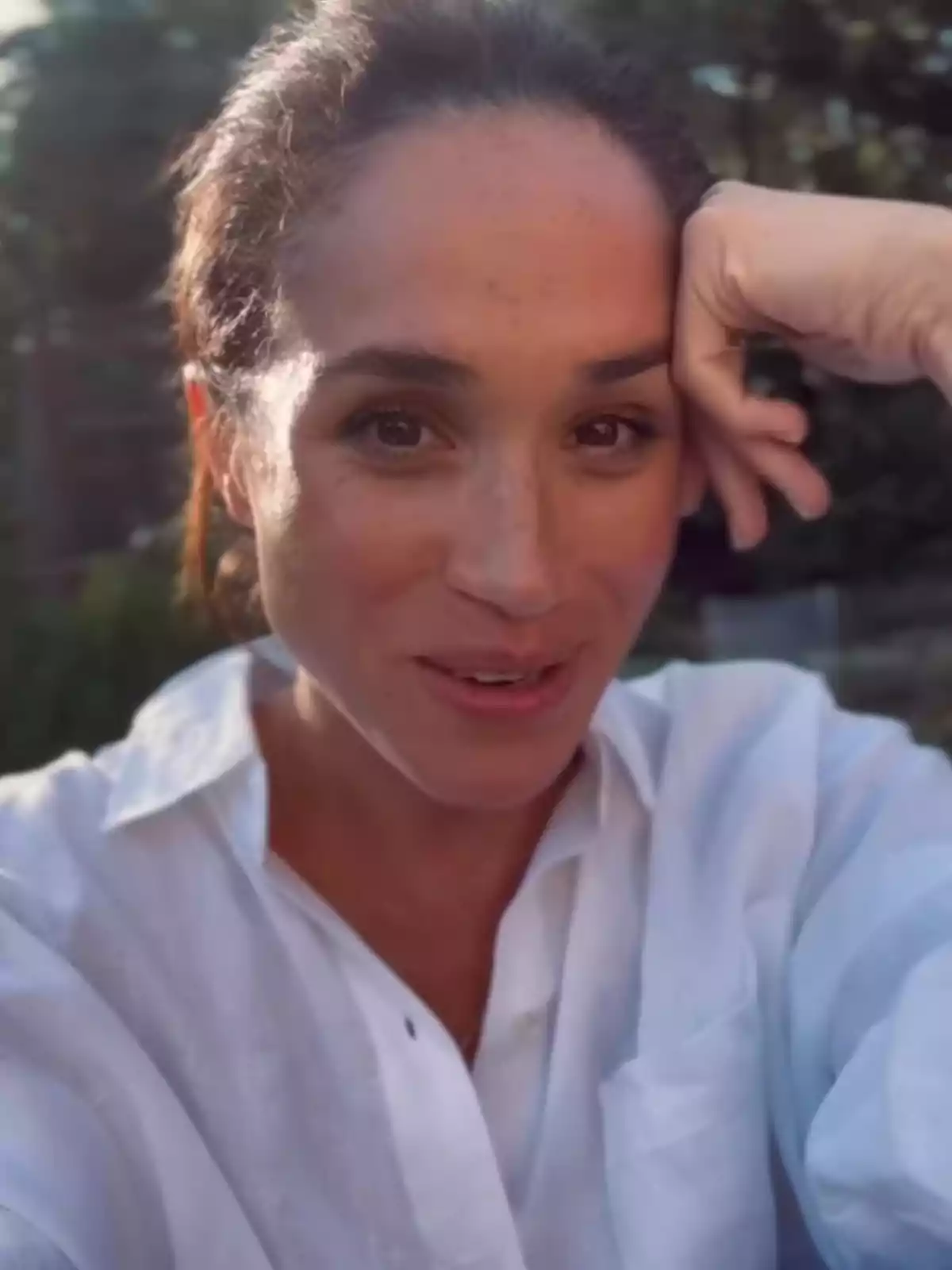 Dona amb camisa blanca somrient i recolzant el cap a la mà en un entorn a l’aire lliure Dona amb camisa blanca somrient i recolzant el cap a la mà en un entorn a l’aire lliure