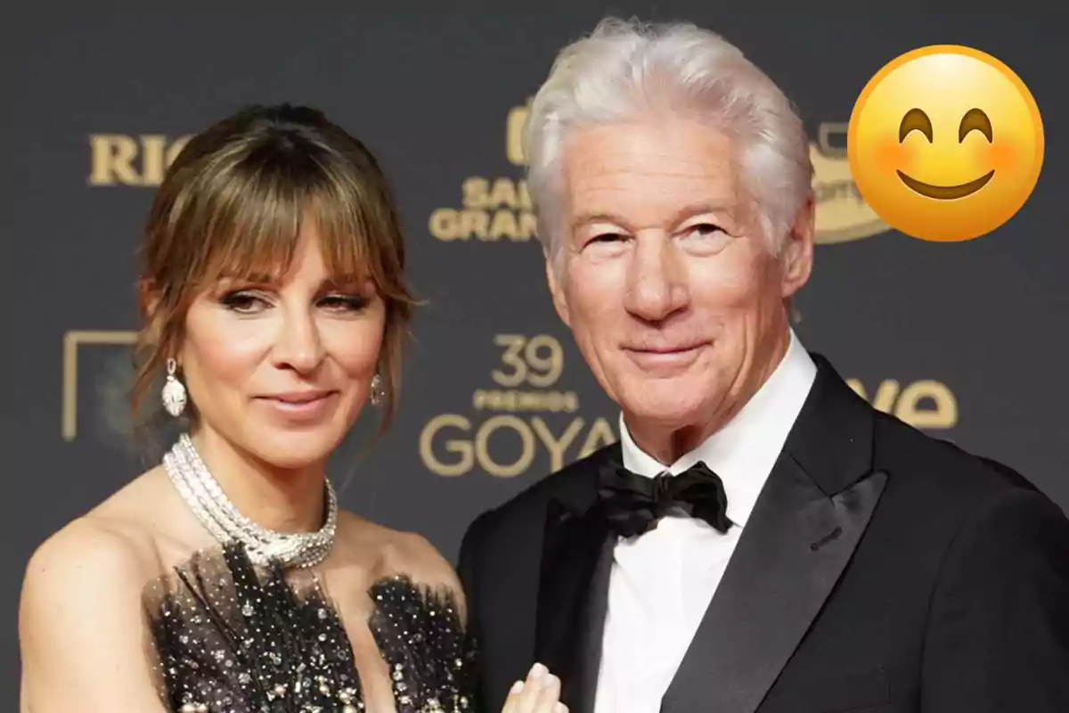 Alejandra Silva and Richard Gere elegantly dressed on a red carpet with a smiling emoji in the top right corner