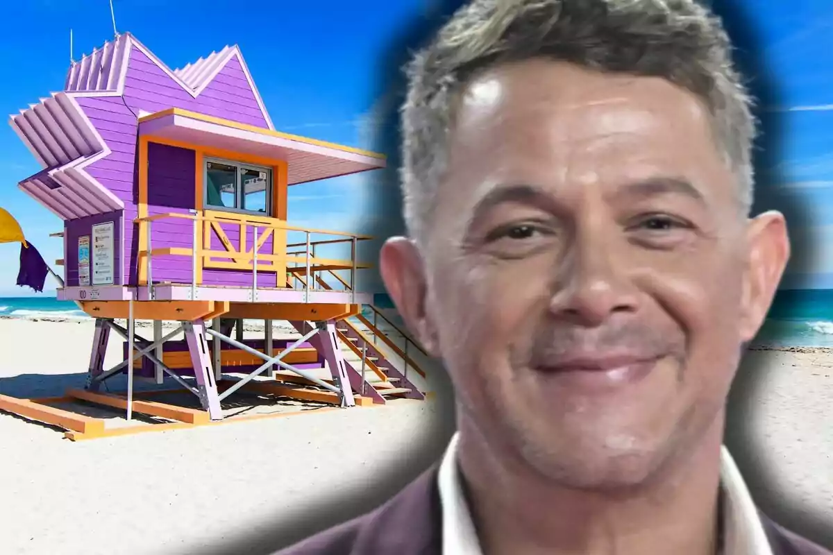 Alejandro Sanz smiling in the foreground with a purple and orange lifeguard hut on the beach in the background