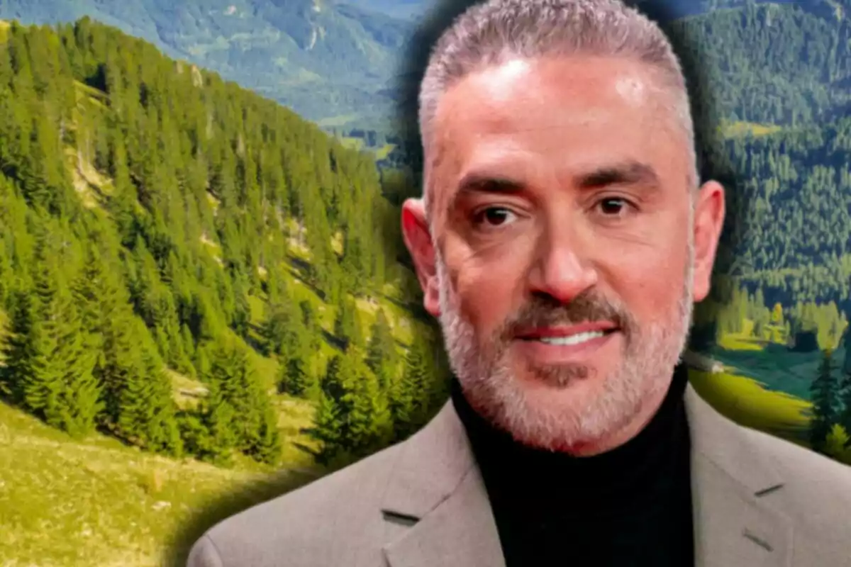 Kiko Hernández amb jaqueta grisa i jersei negre posant davant d’un paisatge de muntanyes i arbres verds