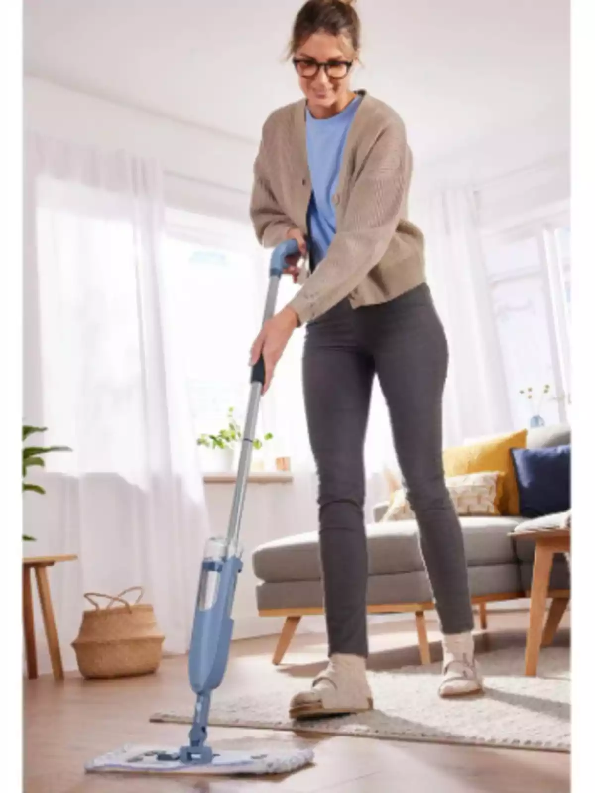 Dona jove netejant el terra d’una sala moderna i lluminosa amb una mopa blava Dona jove netejant el terra d’una sala moderna i lluminosa amb una mopa blava