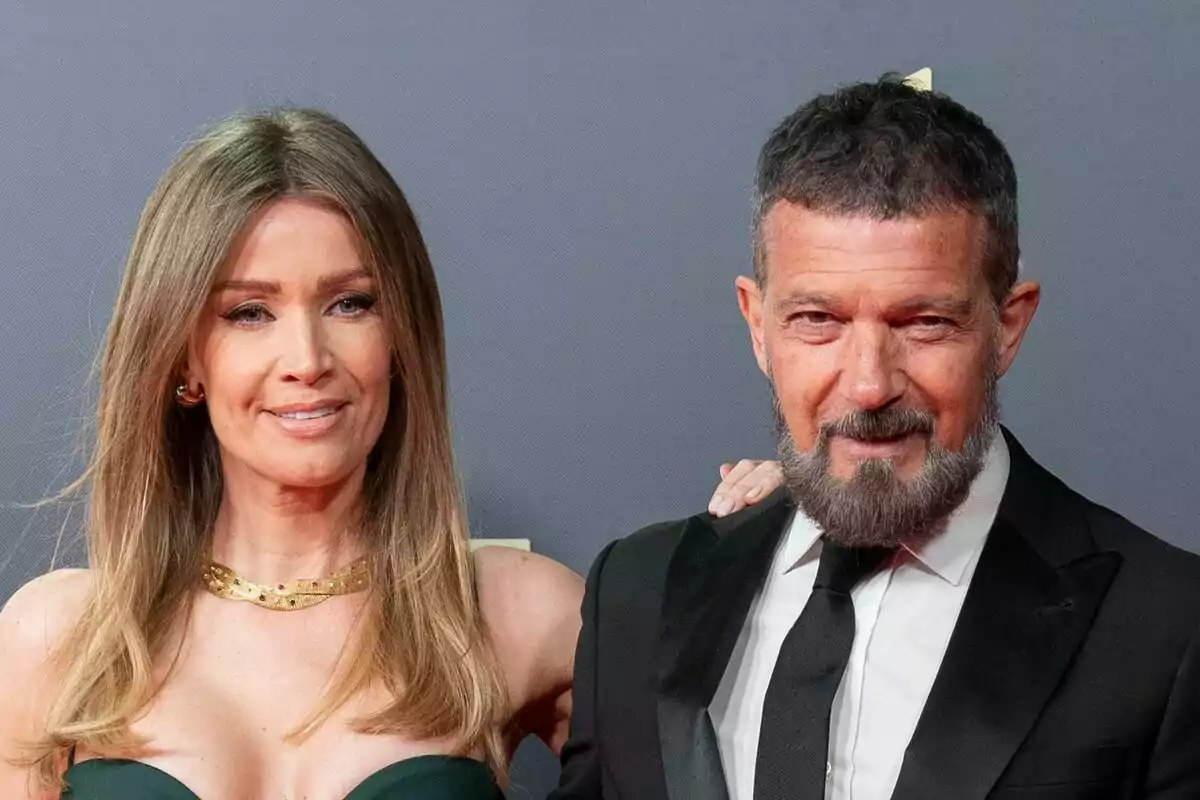 Nicole Kimpel and Antonio Banderas, elegantly dressed, pose smiling on a red carpet in front of a gray background. Nicole Kimpel and Antonio Banderas, elegantly dressed, pose smiling on a red carpet in front of a gray background.
