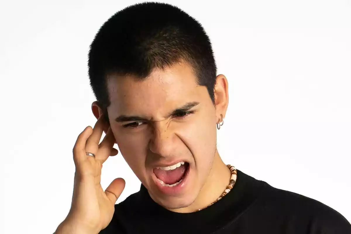 Young man with an annoyed expression holding his hand to his ear and mouth open Young man with an annoyed expression holding his hand to his ear and mouth open