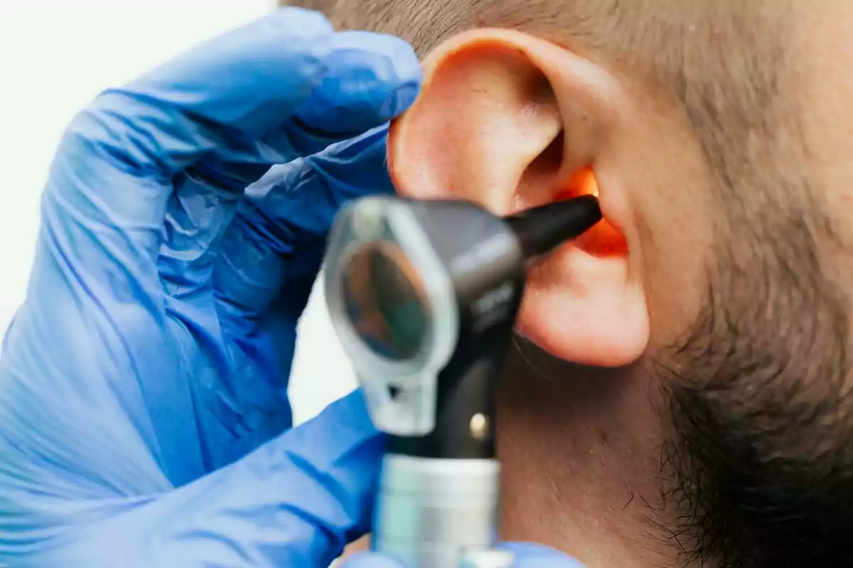 A doctor wearing blue gloves examines a patient's ear using an otoscope. A doctor wearing blue gloves examines a patient's ear using an otoscope.