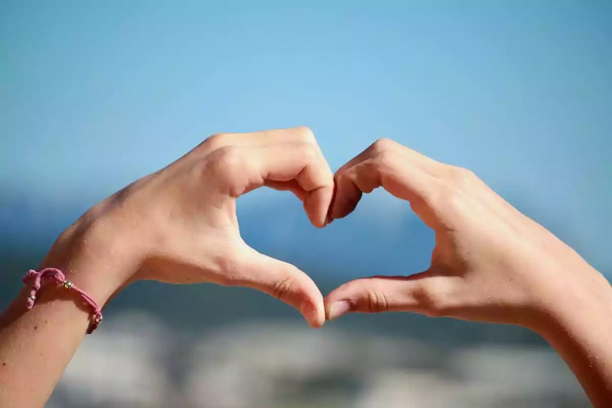 Two hands forming the shape of a heart with the blue sky in the background Two hands forming the shape of a heart with the blue sky in the background