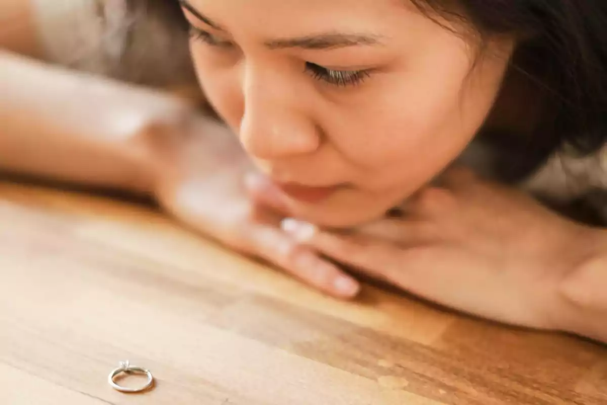 Woman thoughtfully looking at a ring on a wooden table Woman thoughtfully looking at a ring on a wooden table