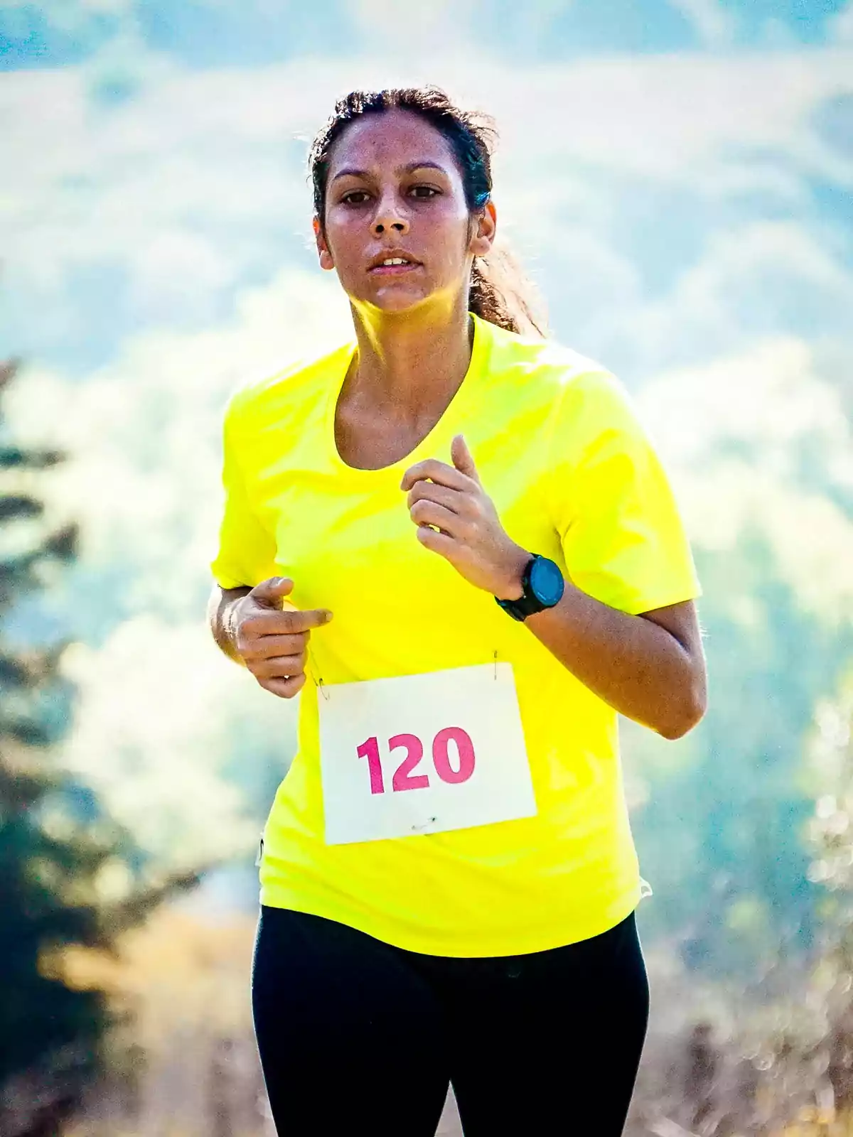 Woman running outdoors wearing a yellow jersey and number 120 in a race Woman running outdoors wearing a yellow jersey and number 120 in a race