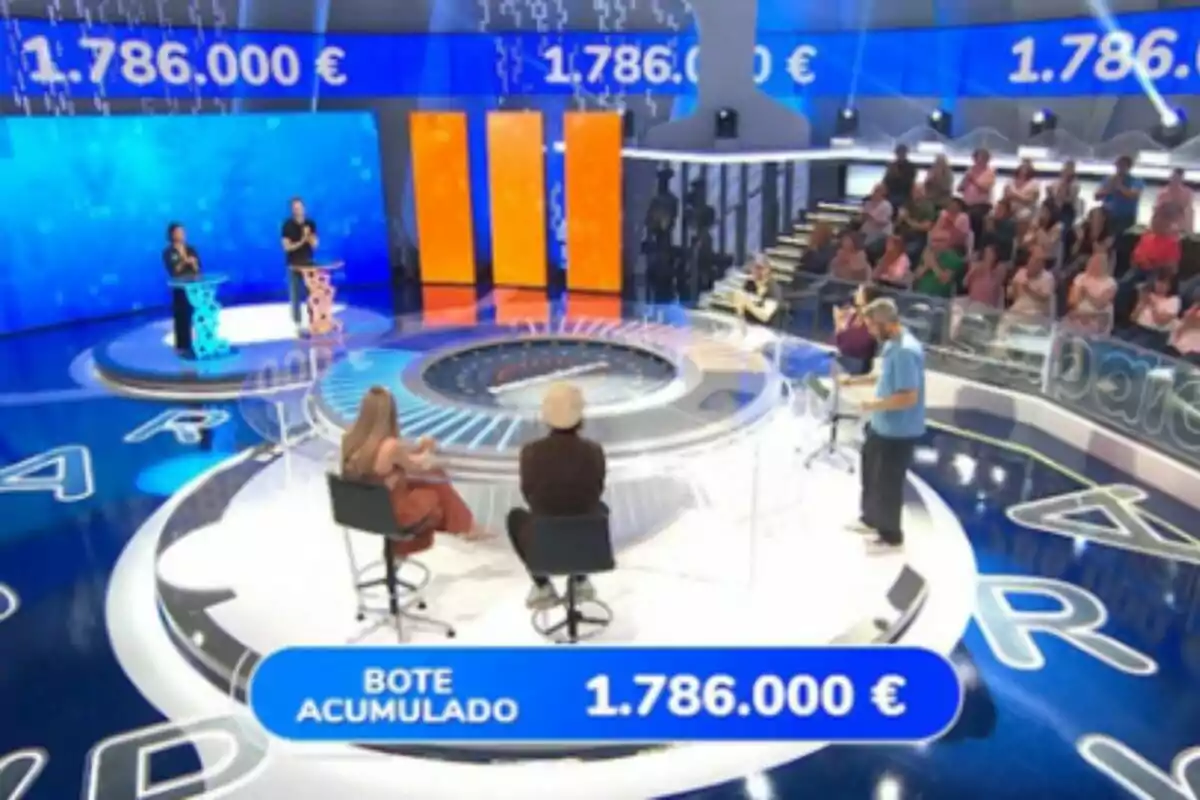 Plató televisiu de 'Pasapalabra' amb participants, públic i un pot acumulat d’un milió set-cents vuitanta-sis mil euros en pantalla. Plató televisiu de 'Pasapalabra' amb participants, públic i un pot acumulat d’un milió set-cents vuitanta-sis mil euros en pantalla.