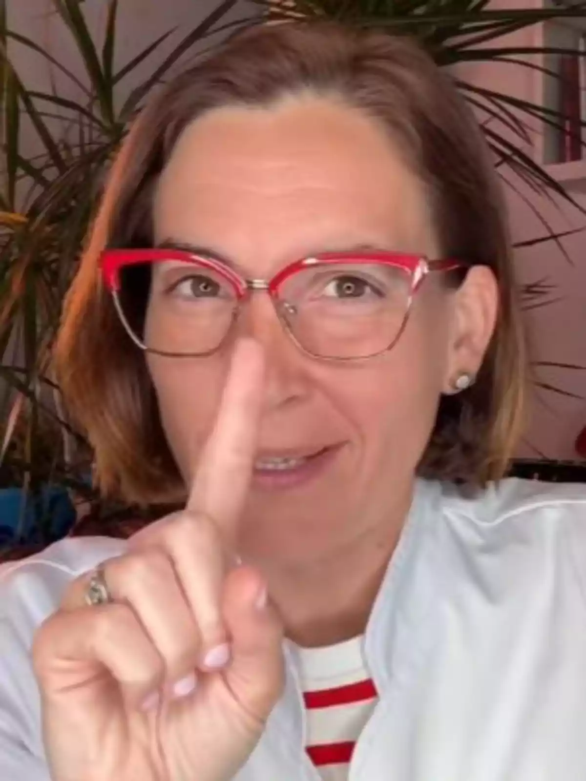 Woman with red glasses pointing upwards with her index finger and smiling