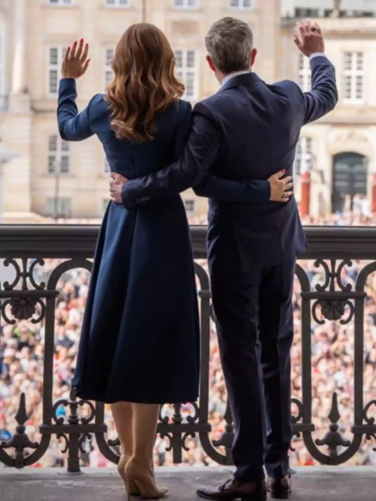 Mary y Federico de Dinamarca elegantemente vestida saluda a una multitud desde un balcón Mary y Federico de Dinamarca elegantemente vestida saluda a una multitud desde un balcón