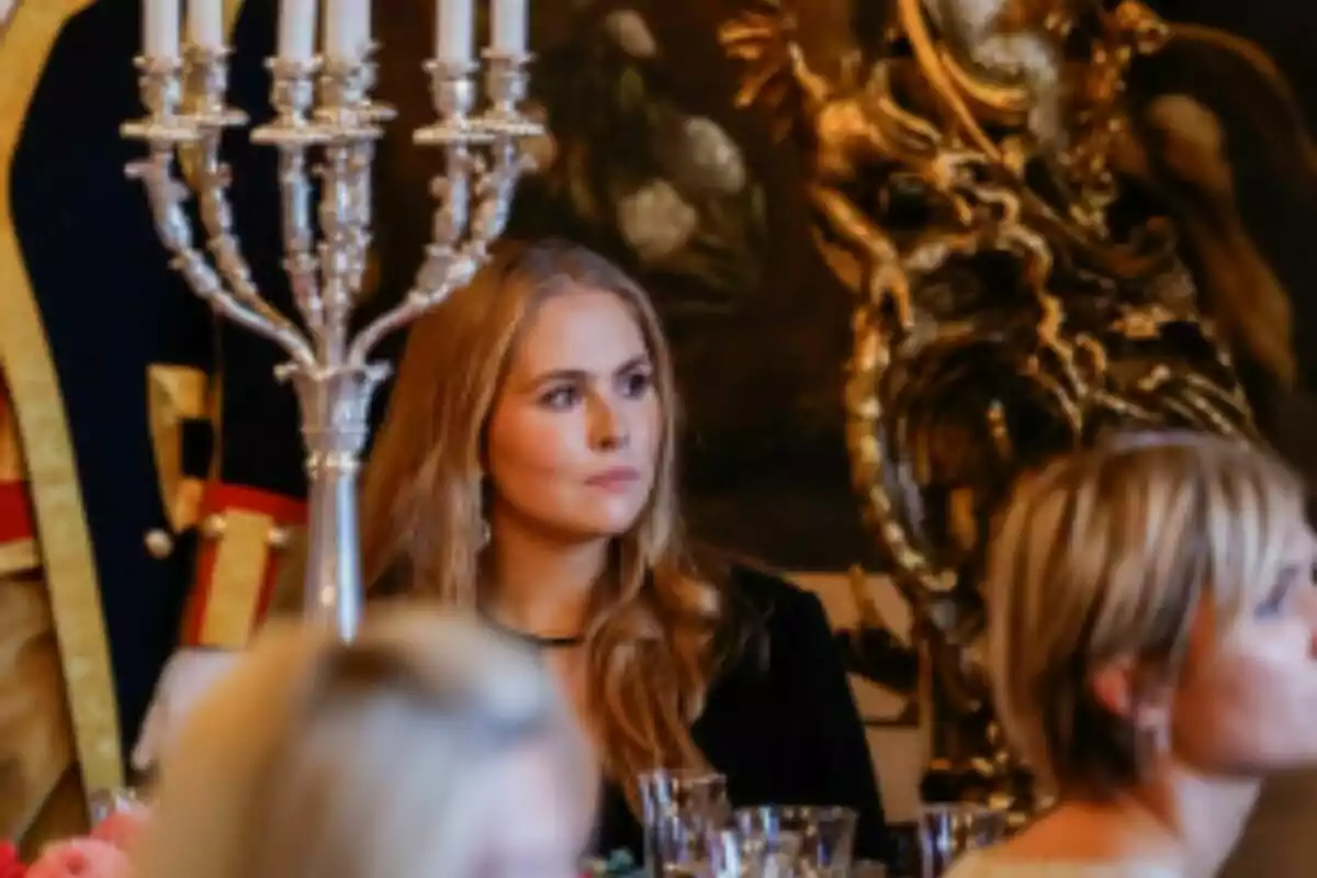 La princesa Amalia asseguda en una taula elegant durant un esdeveniment formal amb un canelobre platejat i decoració daurada al fons.