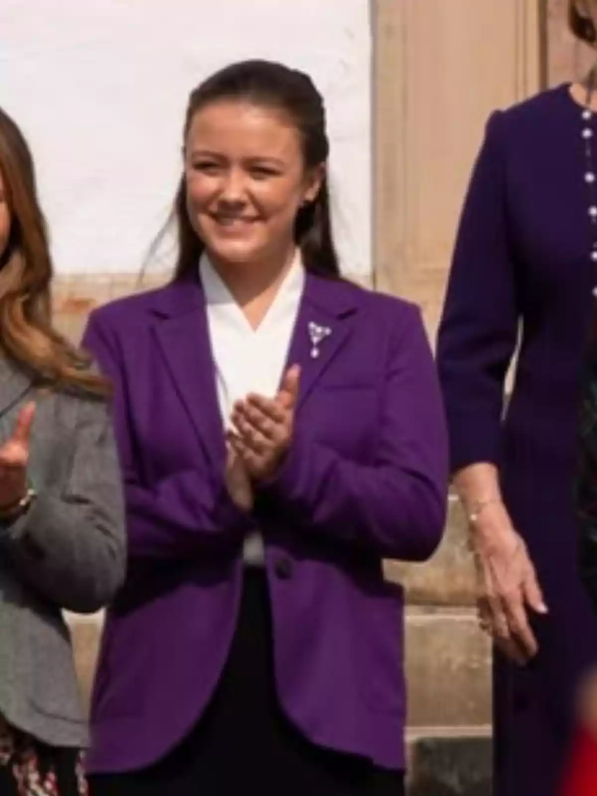 Jove somrient amb jaqueta morada aplaudint dret al costat d’altres persones Jove somrient amb jaqueta morada aplaudint dret al costat d’altres persones