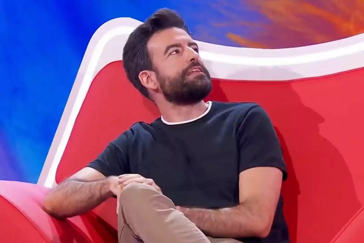 Rafa Castaño amb barba assegut en un sofà vermell mirant cap amunt en un plató d'Agafa't al sofà acolorit Rafa Castaño amb barba assegut en un sofà vermell mirant cap amunt en un plató d'Agafa't al sofà acolorit