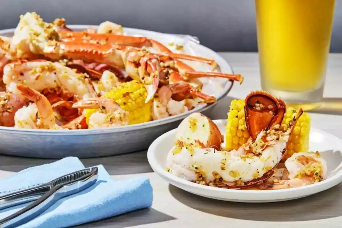 Seafood platter with shrimp, crab, corn, and potato, served with a cold drink and utensils on a blue napkin Seafood platter with shrimp, crab, corn, and potato, served with a cold drink and utensils on a blue napkin