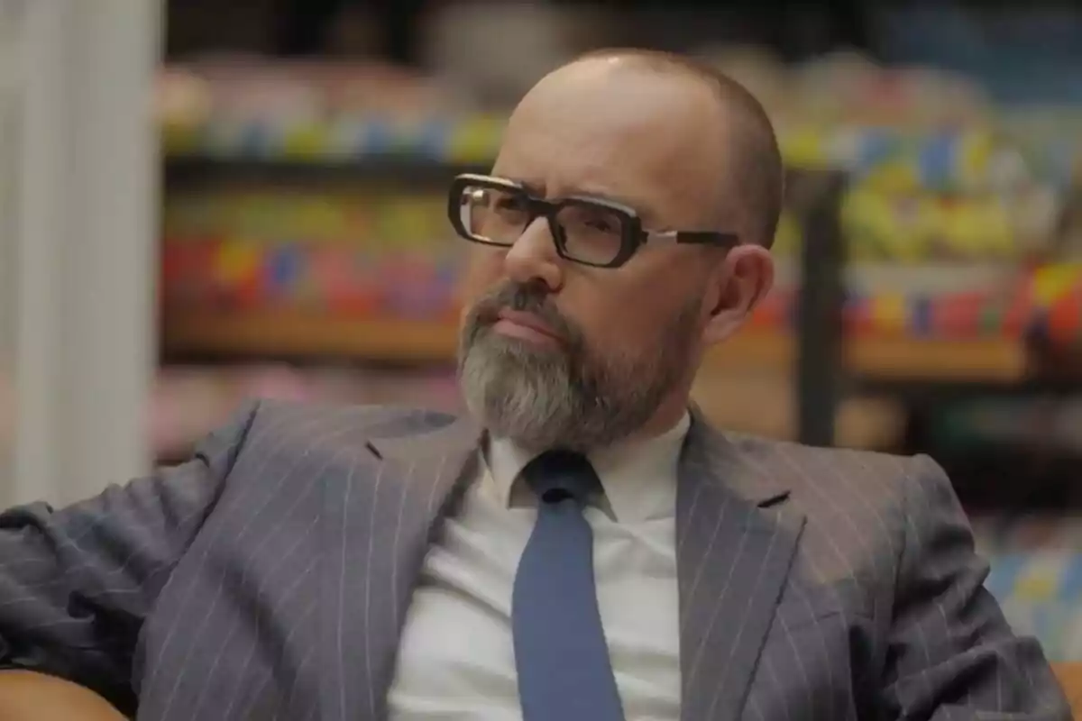 Risto Mejide con barba y gafas de pasta vistiendo un traje de rayas y corbata azul sentado en un ambiente interior desenfocado en 'Viajando con Chester' Risto Mejide con barba y gafas de pasta vistiendo un traje de rayas y corbata azul sentado en un ambiente interior desenfocado en 'Viajando con Chester'