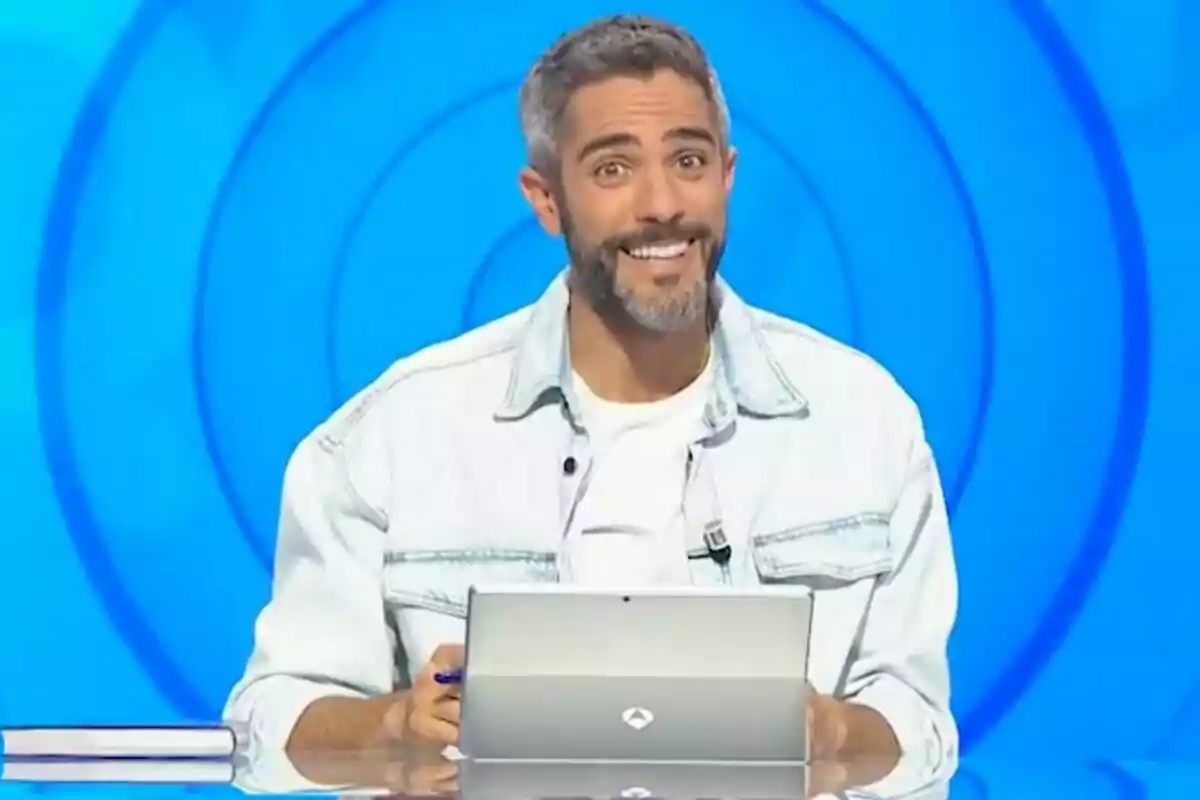 Roberto Leal somrient amb barba i jaqueta clara assegut davant d’una tauleta en un plató de televisió amb fons blau a ‘Pasapalabra’ Roberto Leal somrient amb barba i jaqueta clara assegut davant d’una tauleta en un plató de televisió amb fons blau a ‘Pasapalabra’