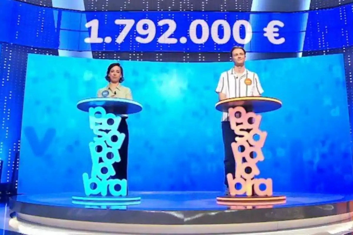 Dos concursants drets en un plató de televisió amb faristols de colors —que són la Rosa i en Manu— i una pantalla al fons que mostra un premi d’un milió set-cents noranta-dos mil euros. Dos concursants drets en un plató de televisió amb faristols de colors —que són la Rosa i en Manu— i una pantalla al fons que mostra un premi d’un milió set-cents noranta-dos mil euros.