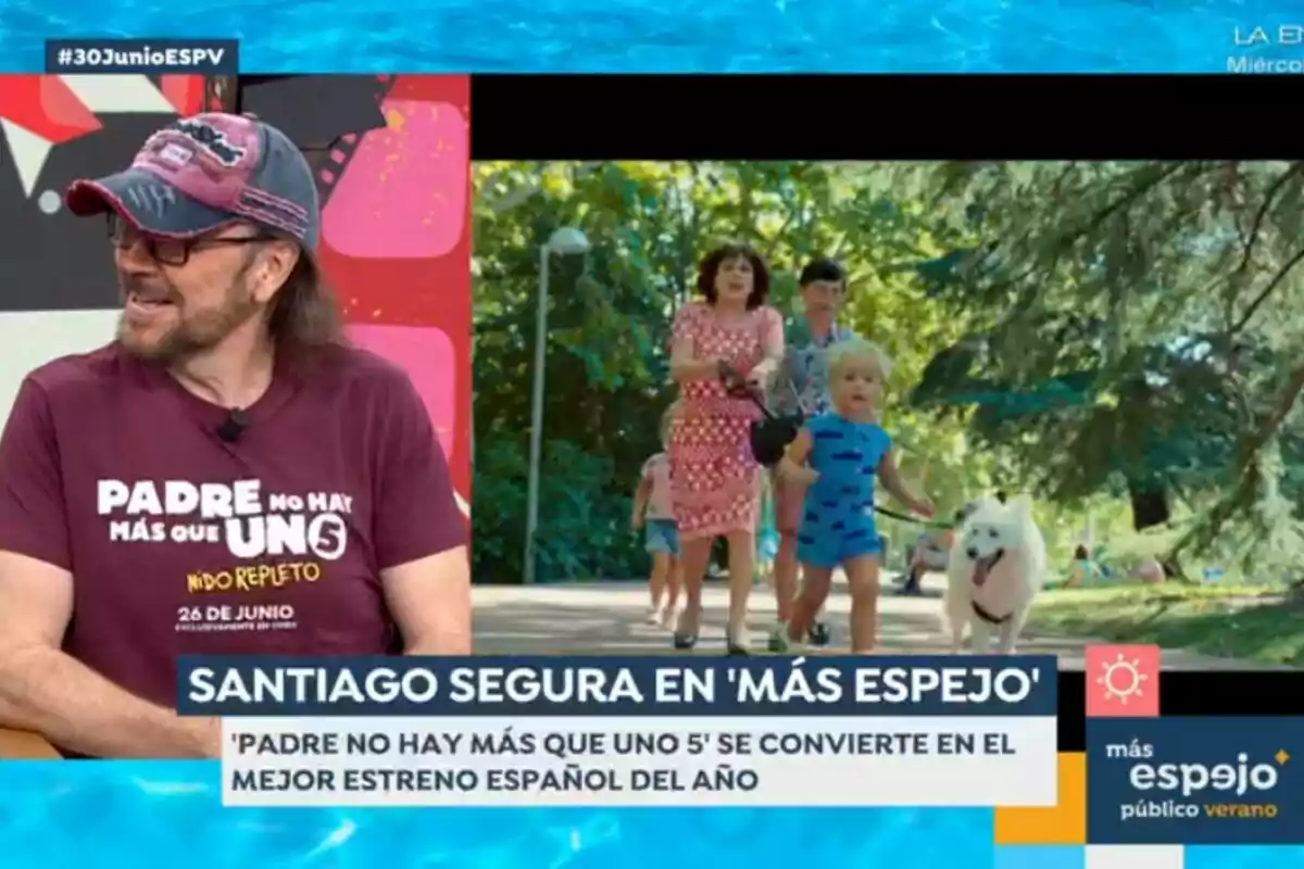 Santiago Segura, wearing a cap and a promotional T-jersey for a movie, is interviewed on a television show while a family scene with children and a dog walking in a park is shown on the screen. Santiago Segura, wearing a cap and a promotional T-jersey for a movie, is interviewed on a television show while a family scene with children and a dog walking in a park is shown on the screen.