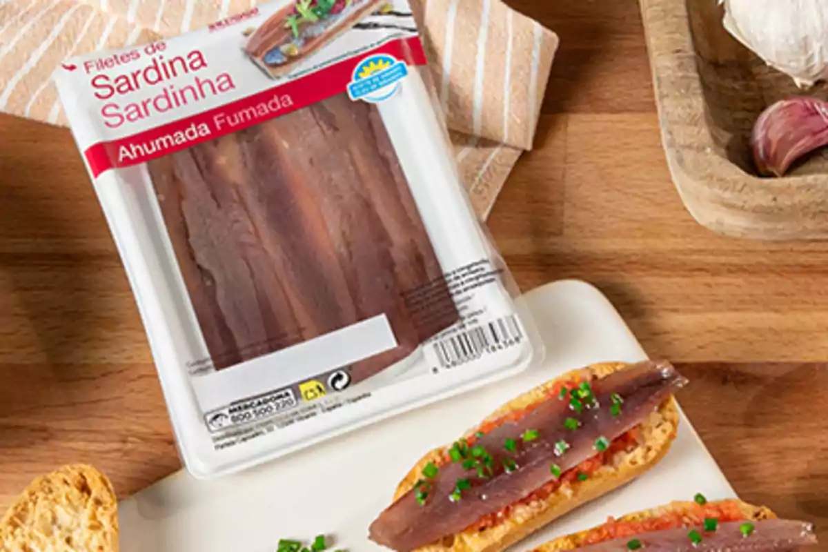 Envàs de filets de sardina fumada al costat de llesques de pa amb tomàquet i sardina sobre una taula de fusta Envàs de filets de sardina fumada al costat de llesques de pa amb tomàquet i sardina sobre una taula de fusta