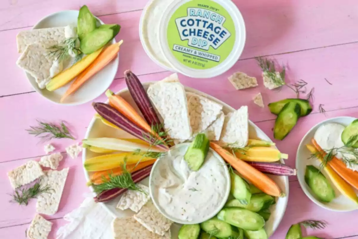 Tray with fresh vegetables, rice cakes, and a cottage cheese dip on a pink table