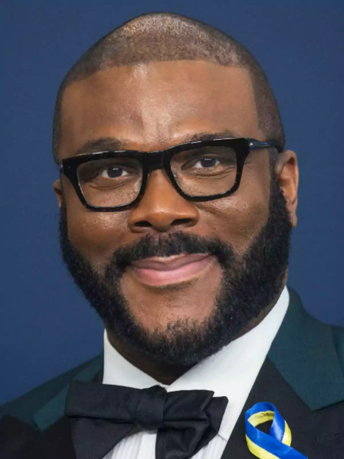 Tyler Perry vestit amb esmòquing i llacet negre amb un llaç blau i groc a la solapa. Tyler Perry vestit amb esmòquing i llacet negre amb un llaç blau i groc a la solapa.