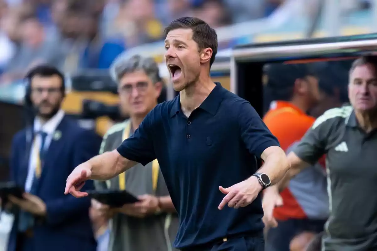 Entrenador de futbol donant indicacions a la banda durant un partit amb expressió intensa i persones de fons observant Entrenador de futbol donant indicacions a la banda durant un partit amb expressió intensa i persones de fons observant