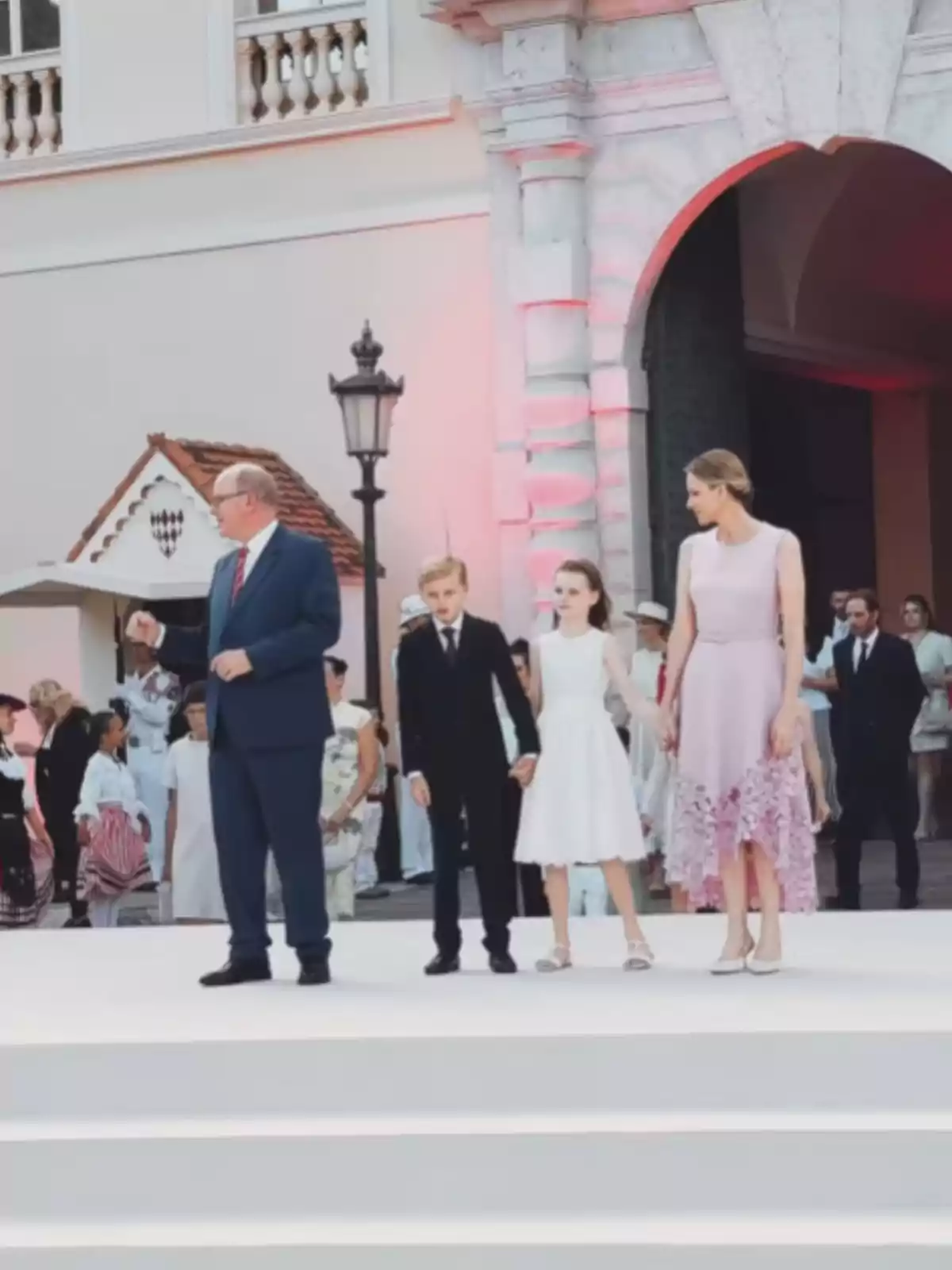 Quatre persones elegantment vestides posen en una escalinata blanca davant d’un edifici històric mentre altres persones observen al fons. Quatre persones elegantment vestides posen en una escalinata blanca davant d’un edifici històric mentre altres persones observen al fons.