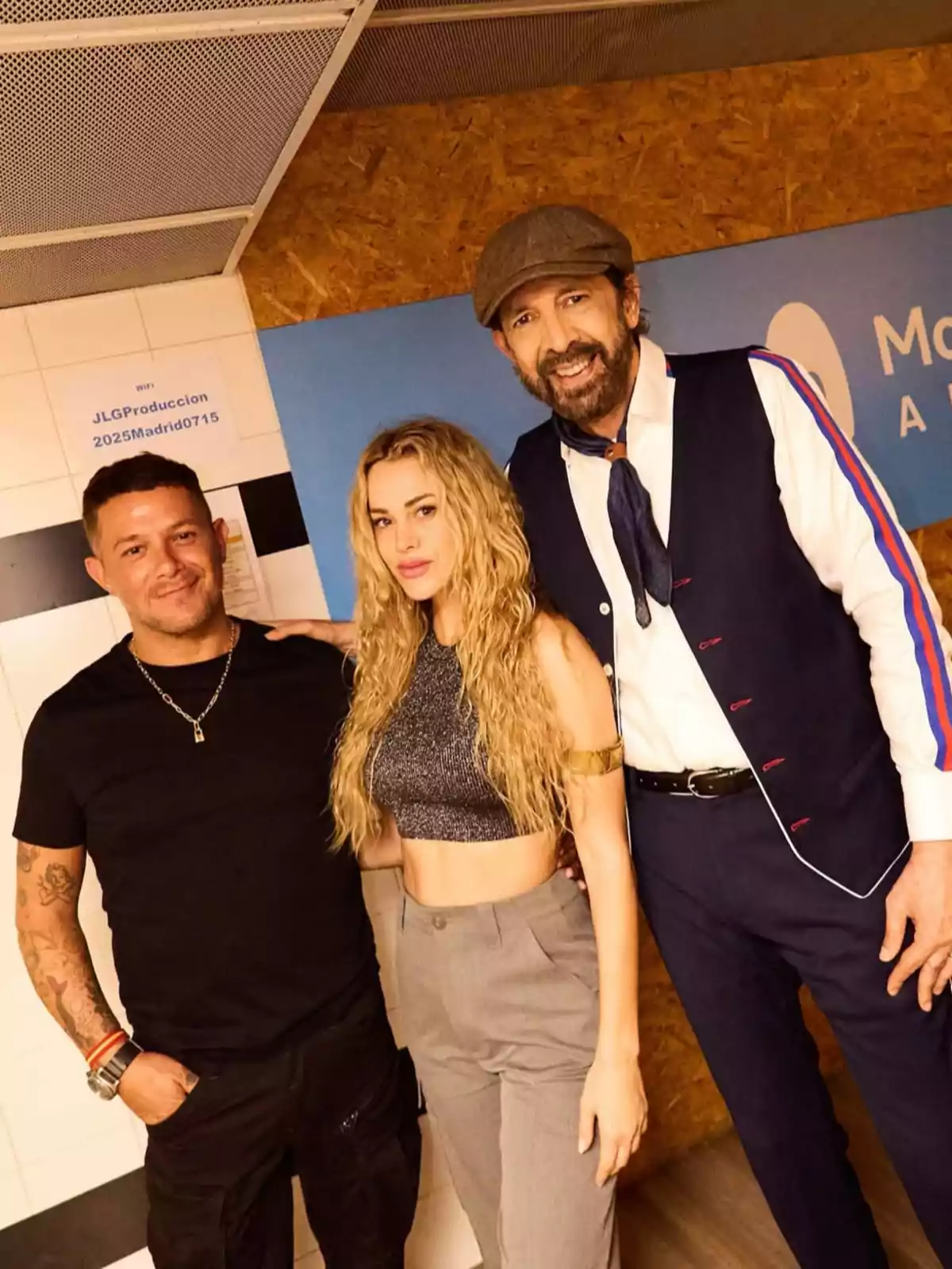 Alejandro Sanz, Candela Márquez, and Juan Luis Guerra pose together and smile in front of a wall with signs; a woman in the center wears a shiny top and gray pants, the man on the left is wearing a black t-jersey, and the man on the right is dressed in a blue suit with a beret. Alejandro Sanz, Candela Márquez, and Juan Luis Guerra pose together and smile in front of a wall with signs; a woman in the center wears a shiny top and gray pants, the man on the left is wearing a black t-jersey, and the man on the right is dressed in a blue suit with a beret.