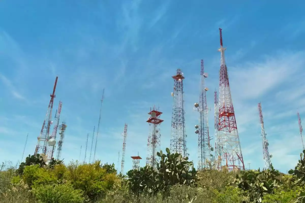 Varias antenas de telecomunicaciones de diferentes tamaños y colores se elevan sobre una zona con vegetación bajo un cielo azul Varias antenas de telecomunicaciones de diferentes tamaños y colores se elevan sobre una zona con vegetación bajo un cielo azul