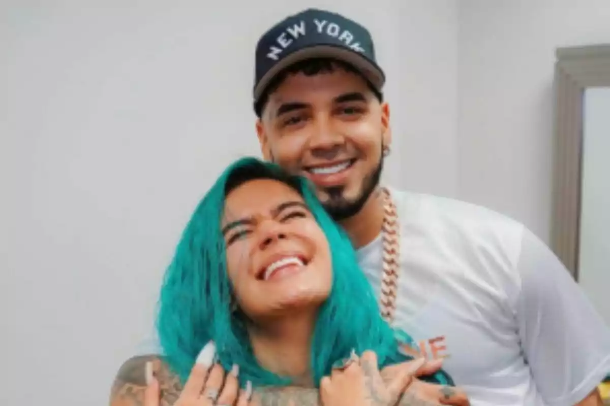 Pareja abrazándose y sonriendo, que son Karol G y Anuel AA, la mujer tiene el cabello azul y el hombre lleva una gorra negra que dice New York. Pareja abrazándose y sonriendo, que son Karol G y Anuel AA, la mujer tiene el cabello azul y el hombre lleva una gorra negra que dice New York.
