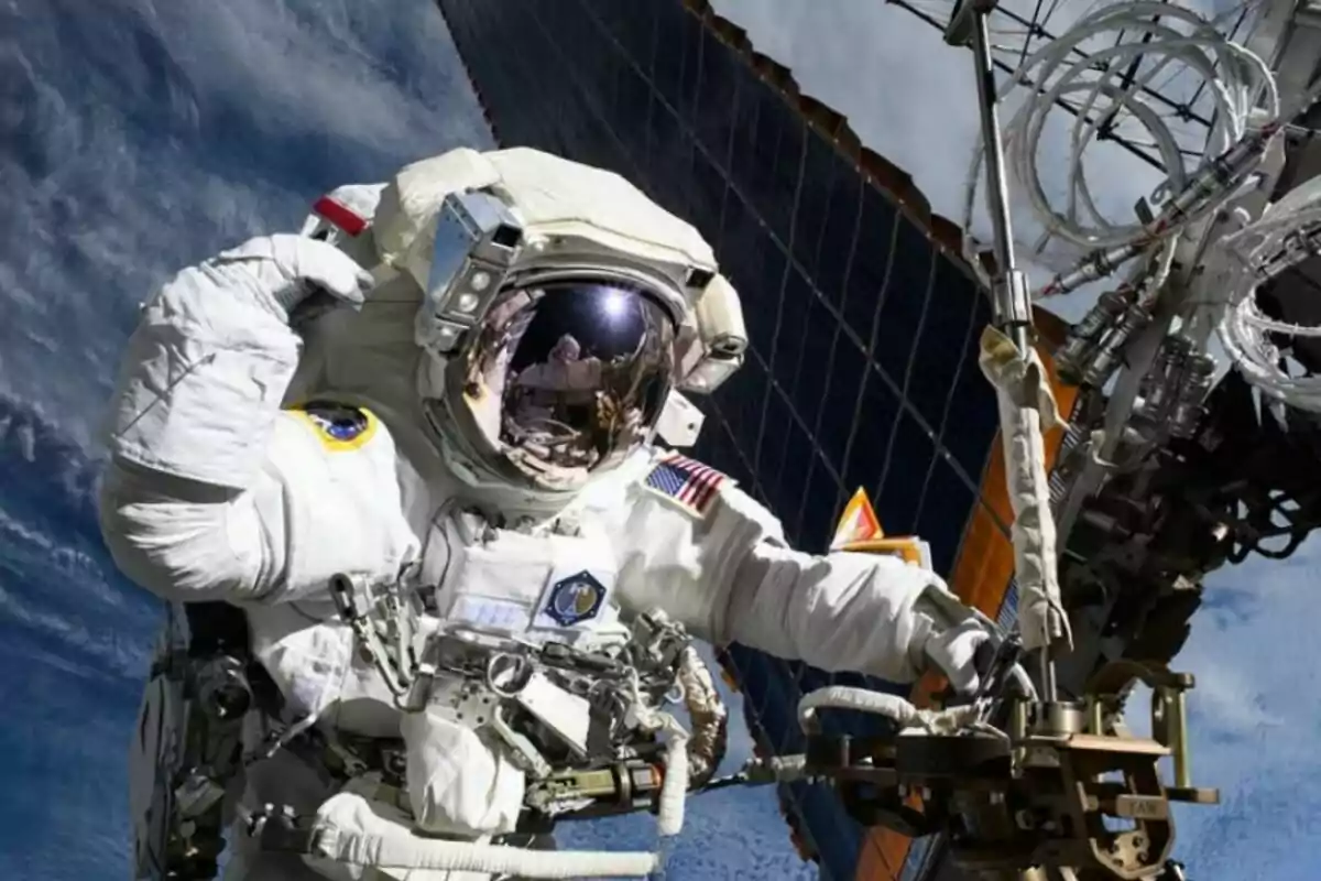 Astronauta realizando una caminata espacial junto a una estructura metálica y paneles solares con la Tierra de fondo