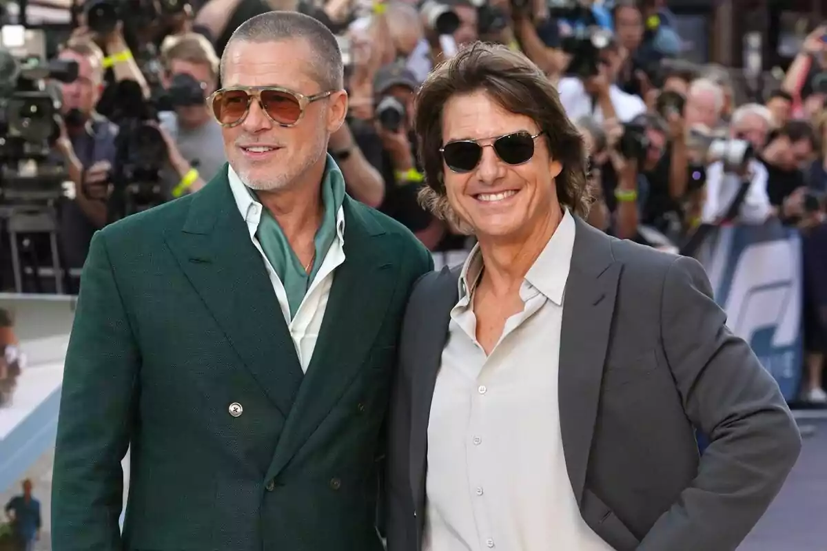 Dos hombres con gafas de sol y trajes elegantes, que son Brad Pitt y Tom Cruise, posan sonrientes en una alfombra roja rodeados de fotógrafos y público. Dos hombres con gafas de sol y trajes elegantes, que son Brad Pitt y Tom Cruise, posan sonrientes en una alfombra roja rodeados de fotógrafos y público.