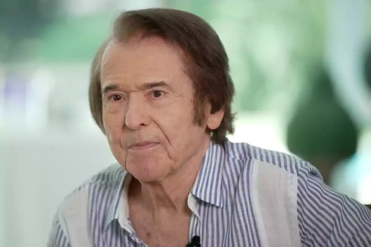 Rapahel amb camisa de ratlles assegut en un ambient il·luminat durant una entrevista Rapahel amb camisa de ratlles assegut en un ambient il·luminat durant una entrevista