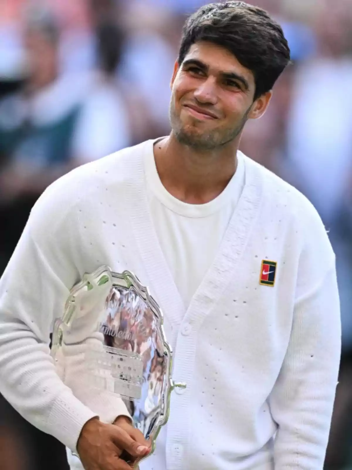 Jove tennista somrient amb jersei blanc sosté un trofeu platejat en una cerimònia esportiva Jove tennista somrient amb jersei blanc sosté un trofeu platejat en una cerimònia esportiva