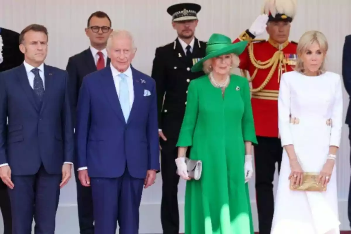 Quatre persones elegantment vestides posen per a una foto oficial al costat de membres del personal de seguretat i un guàrdia amb uniforme vermell. Quatre persones elegantment vestides posen per a una foto oficial al costat de membres del personal de seguretat i un guàrdia amb uniforme vermell.