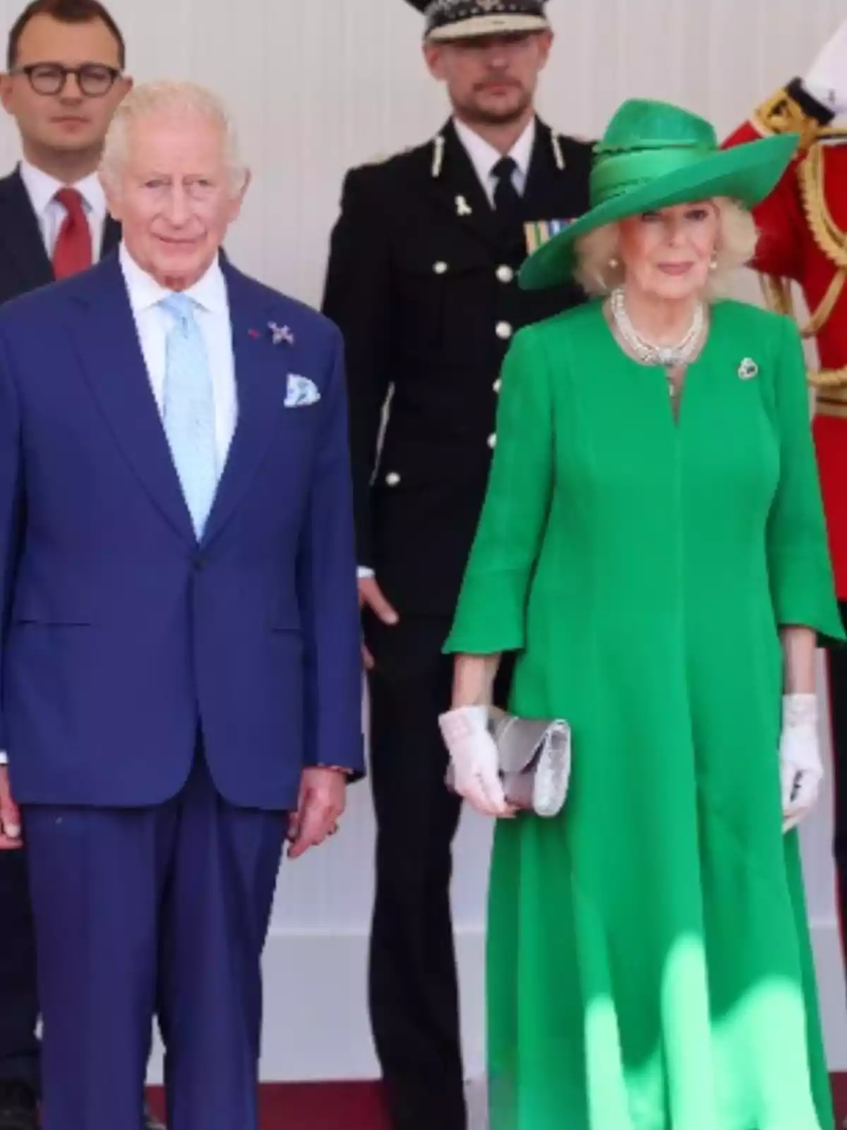 Parella elegantament vestida posant en un esdeveniment formal amb persones uniformades al fons Parella elegantament vestida posant en un esdeveniment formal amb persones uniformades al fons