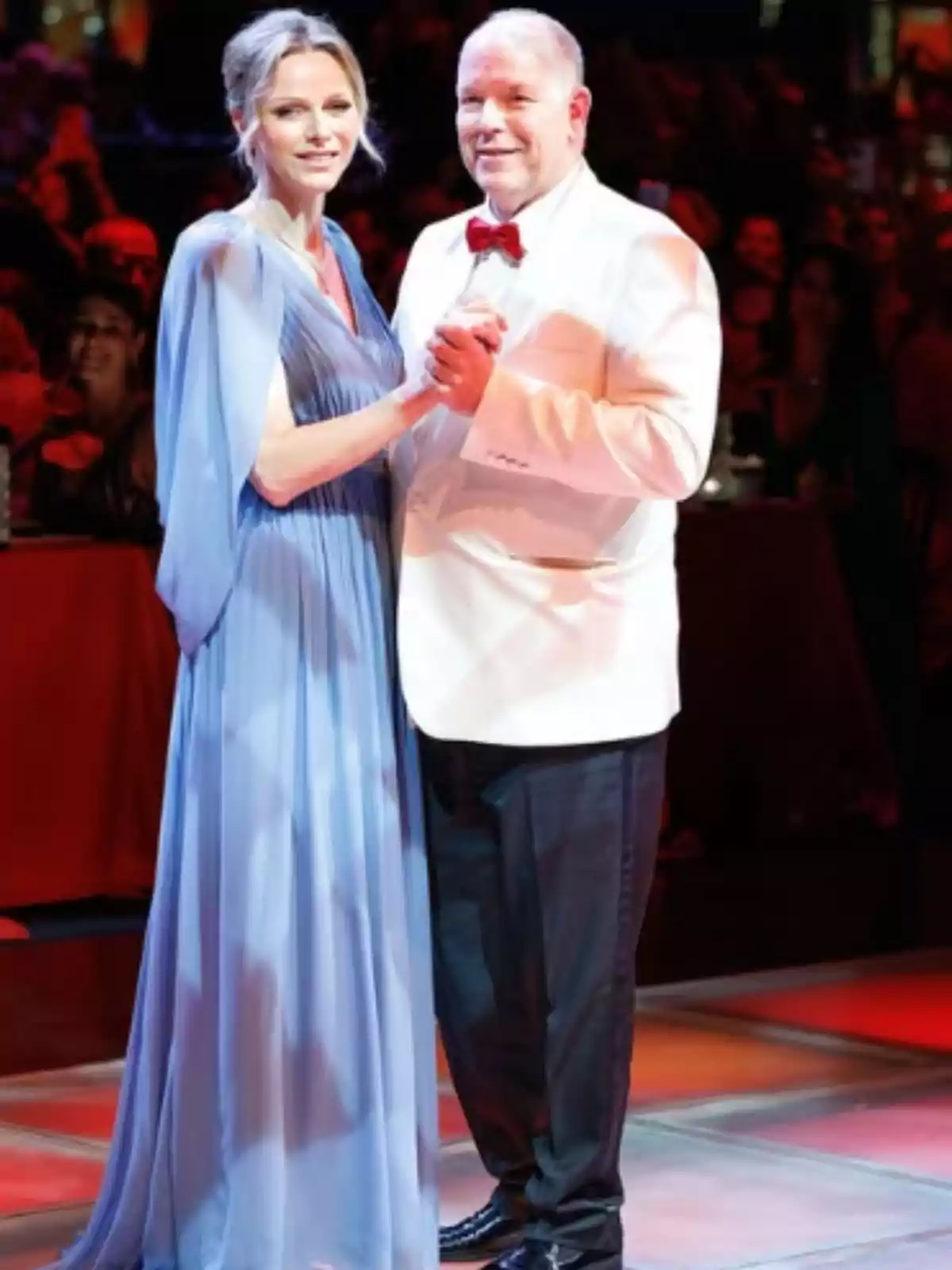 Una parella elegantament vestida balla en un esdeveniment formal amb llums càlides i públic al fons Una parella elegantament vestida balla en un esdeveniment formal amb llums càlides i públic al fons
