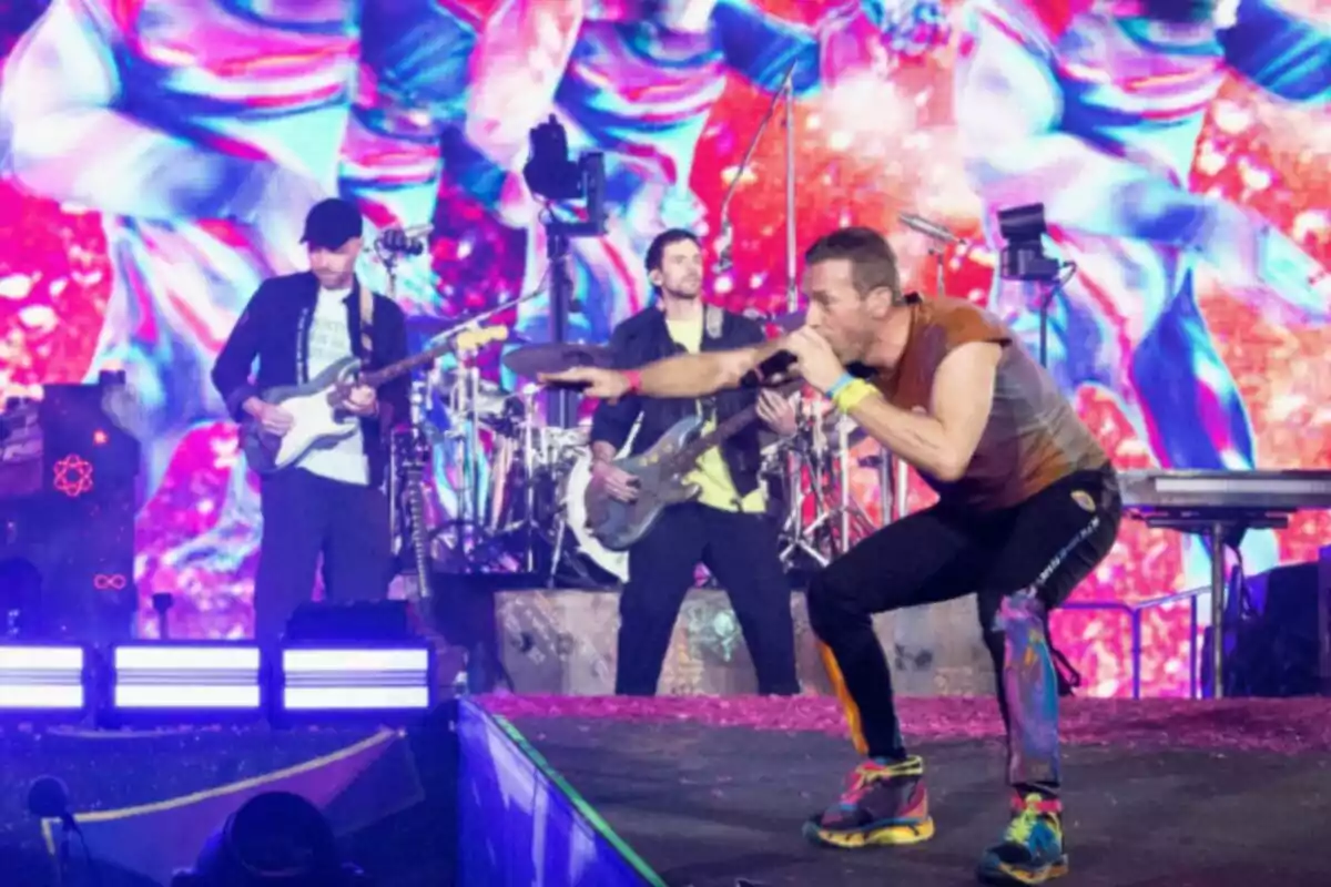 Banda de música tocando en un escenario con luces y fondo colorido mientras el vocalista canta y se inclina hacia el público Banda de música tocando en un escenario con luces y fondo colorido mientras el vocalista canta y se inclina hacia el público