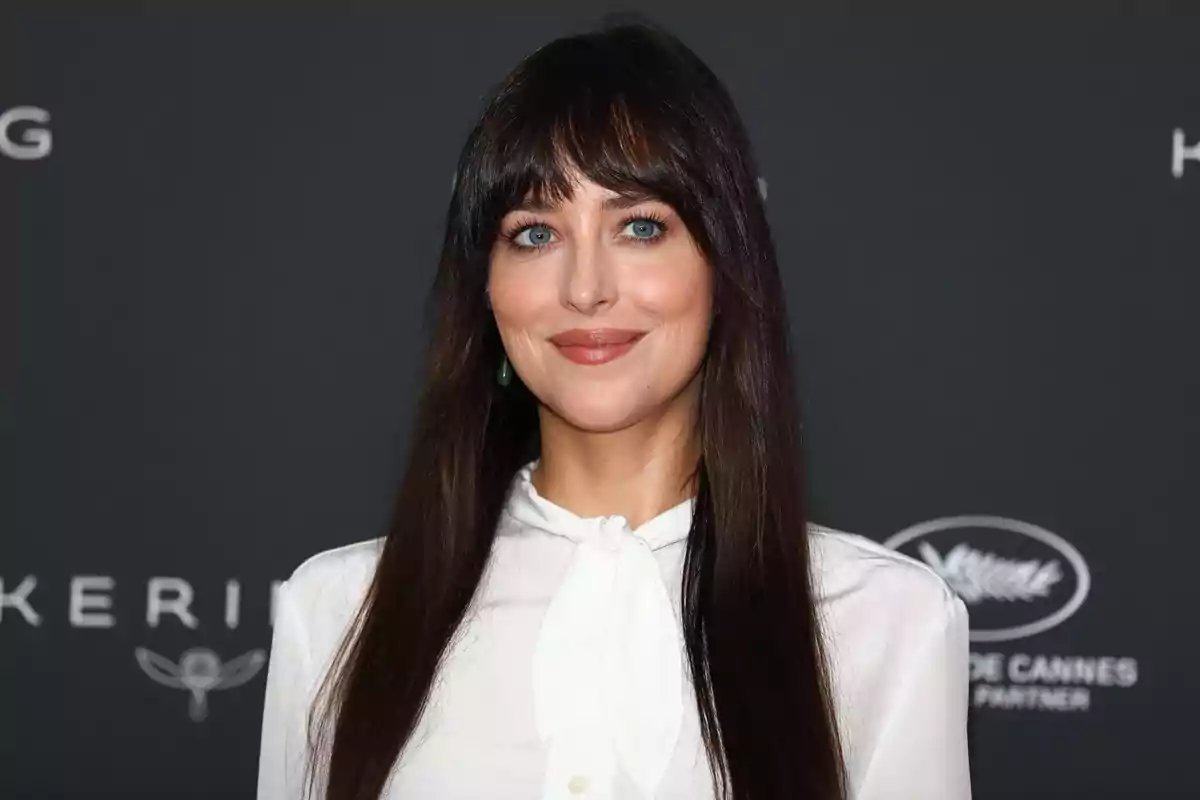 Dakota Johnson, wearing a white blouse and posing in front of a gray background at a formal event Dakota Johnson, wearing a white blouse and posing in front of a gray background at a formal event